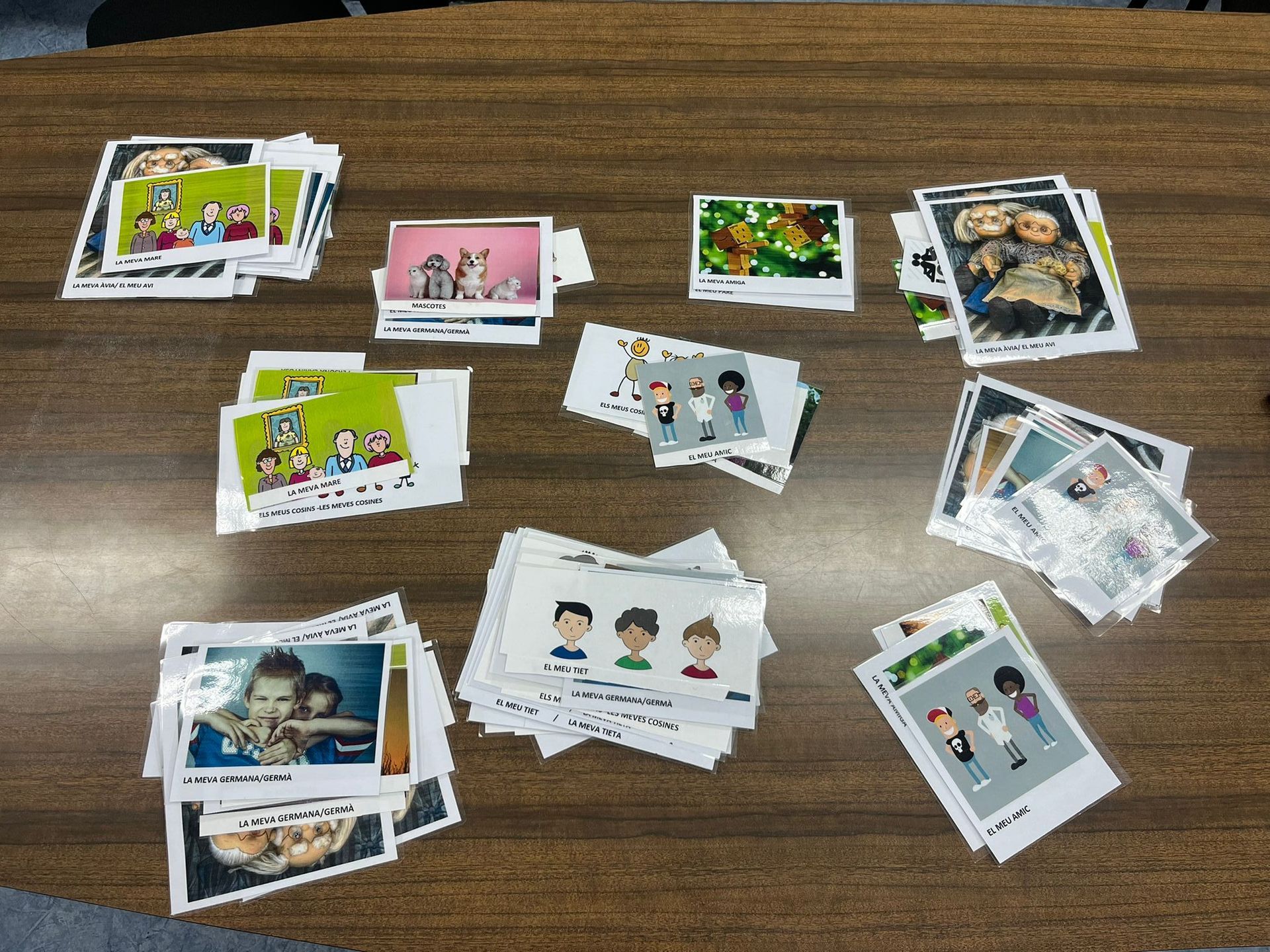 Piles de targetes fotogràfiques de colors sobre una taula de fusta, amb persones de dibuixos animats i fotos de la vida real.