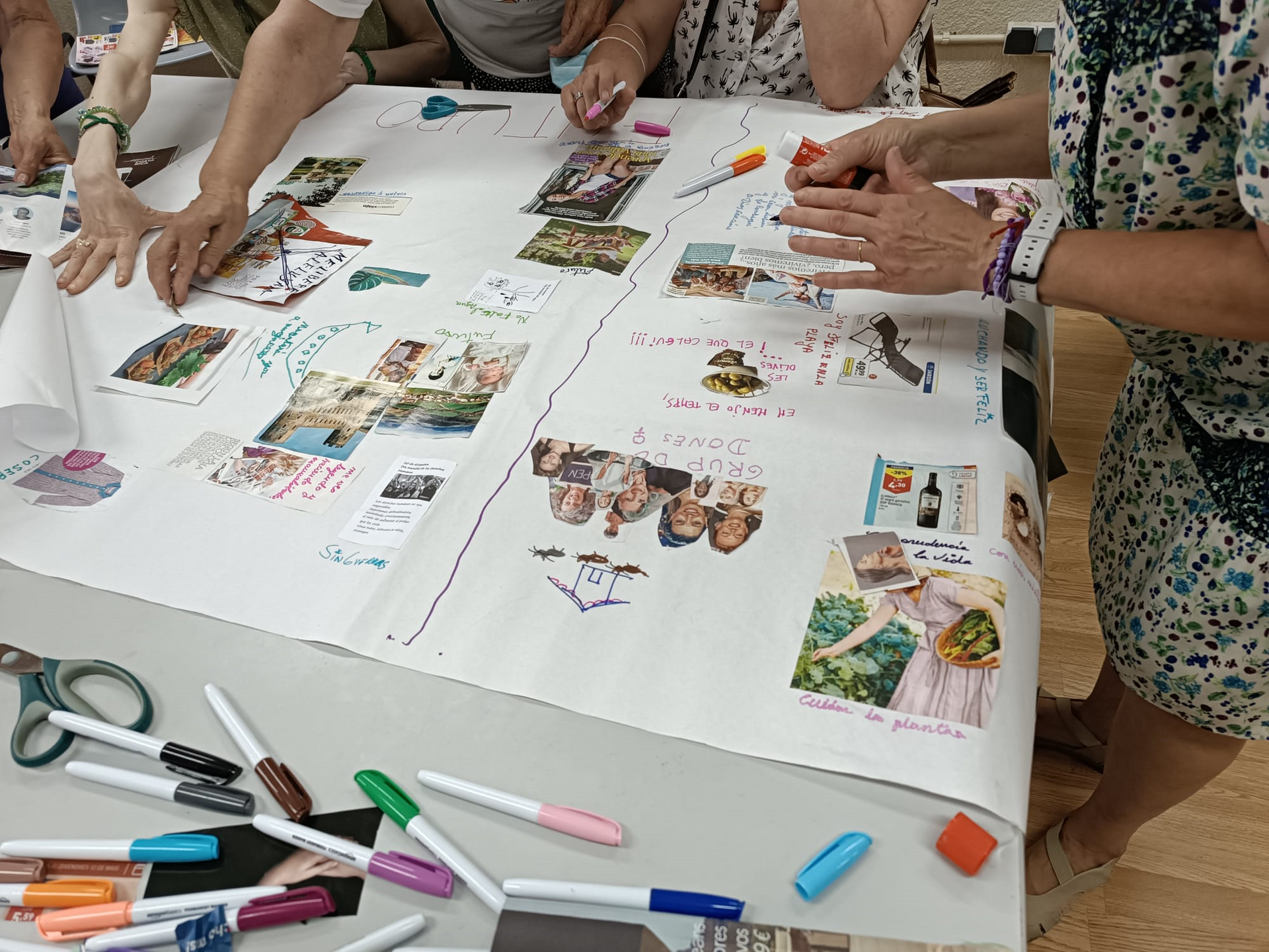 Gent creant un tauler de visió en un full de paper gran, utilitzant fotos, retoladors i tisores.