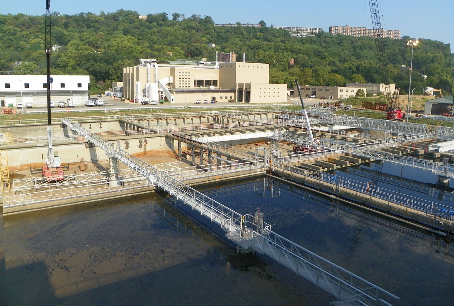 Water treatment plant with tanks, walkways, and a large building. Hills are in the background.
