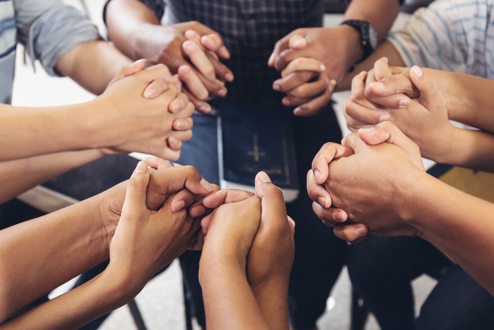 Hands clasped in prayer, surrounding a Bible.