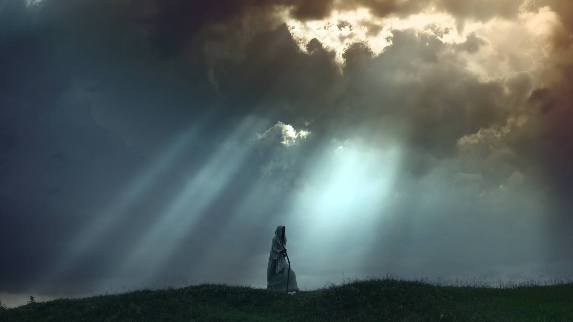 Stone monolith on a grassy hill, with dramatic sunlight breaking through stormy clouds.