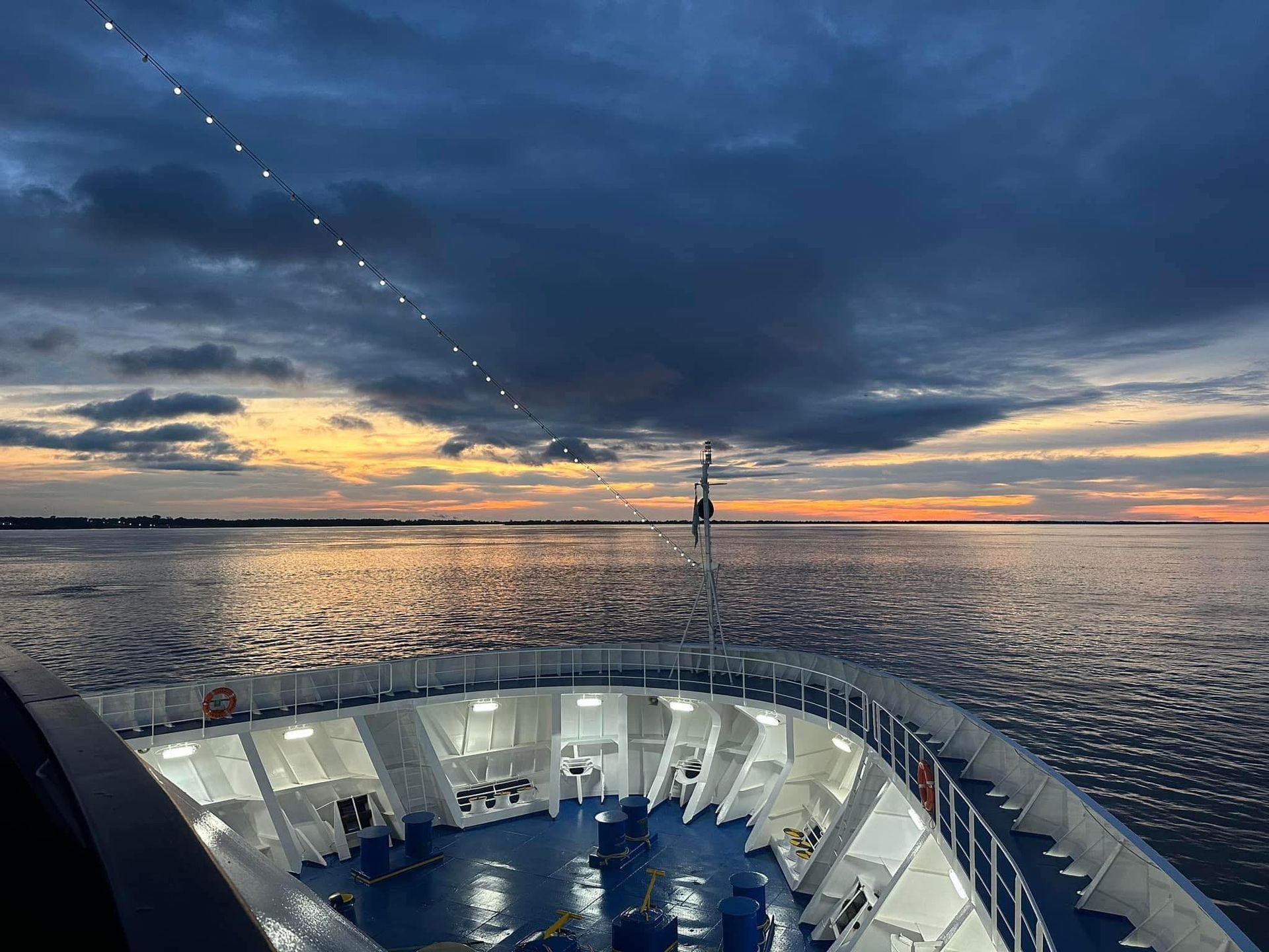 Bow of a ship at sunset, orange and dark blue sky reflects on the water.