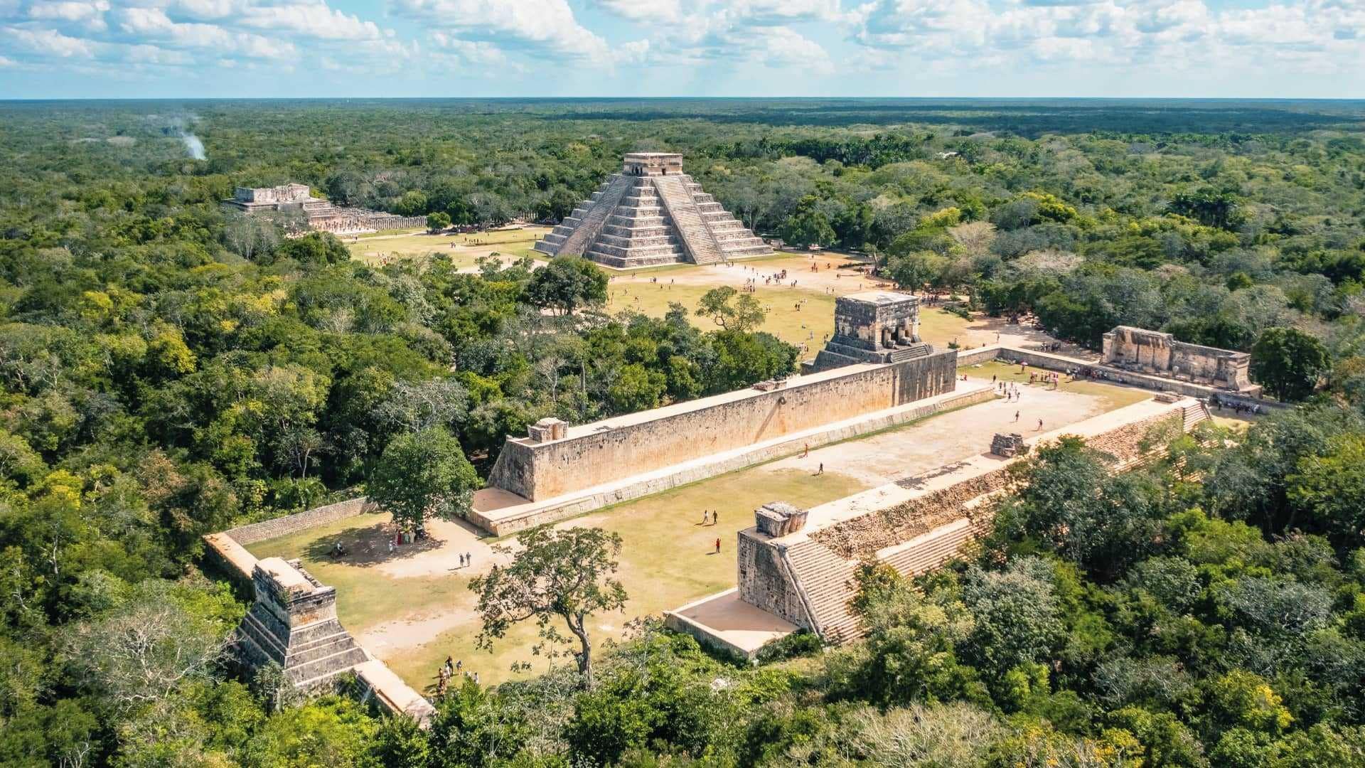 Aerial view of Chichen Itza, Mexico. The El Castillo pyramid is visible with structures surrounded by green trees.