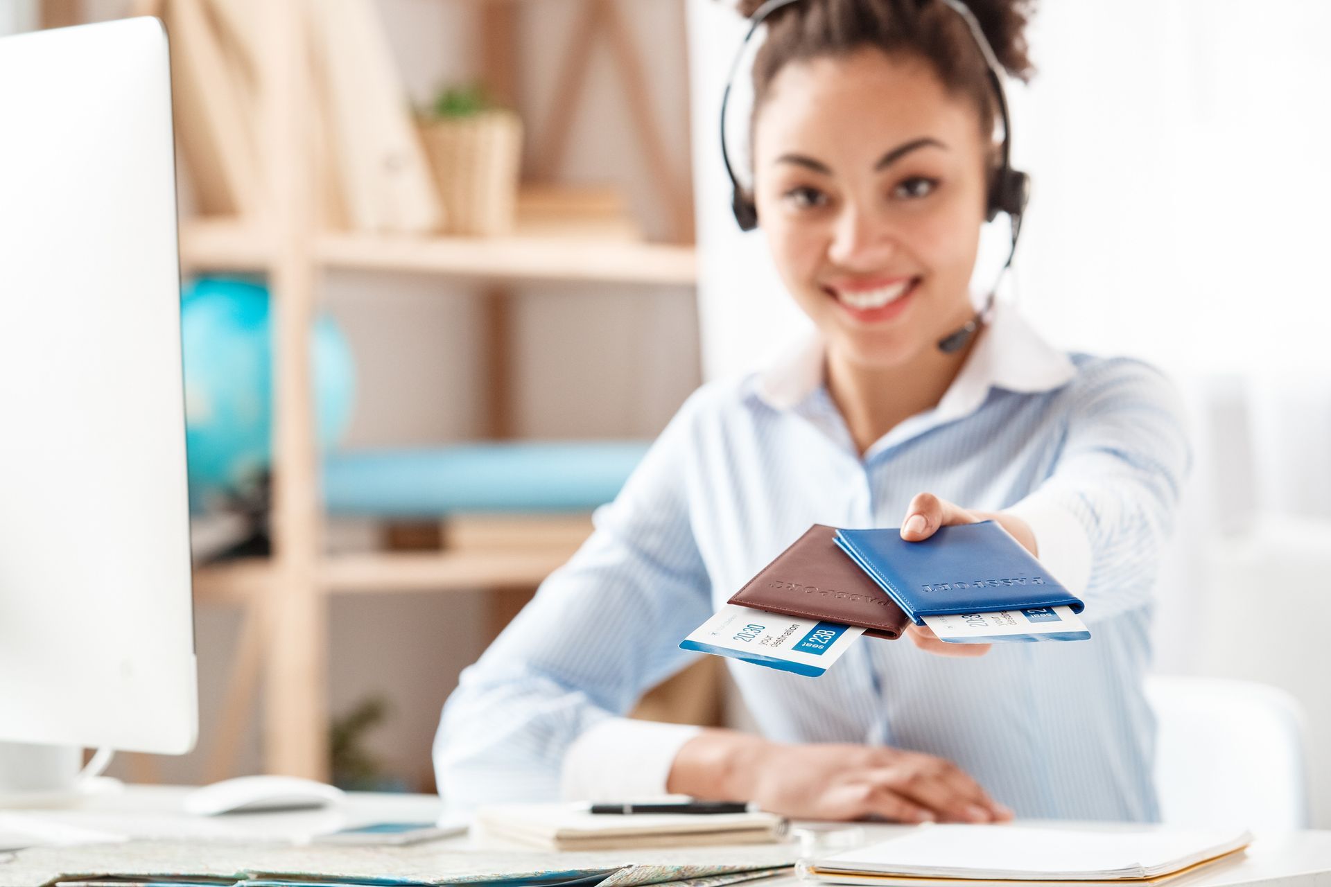 Woman with headset holding out passports, smiling at desk.