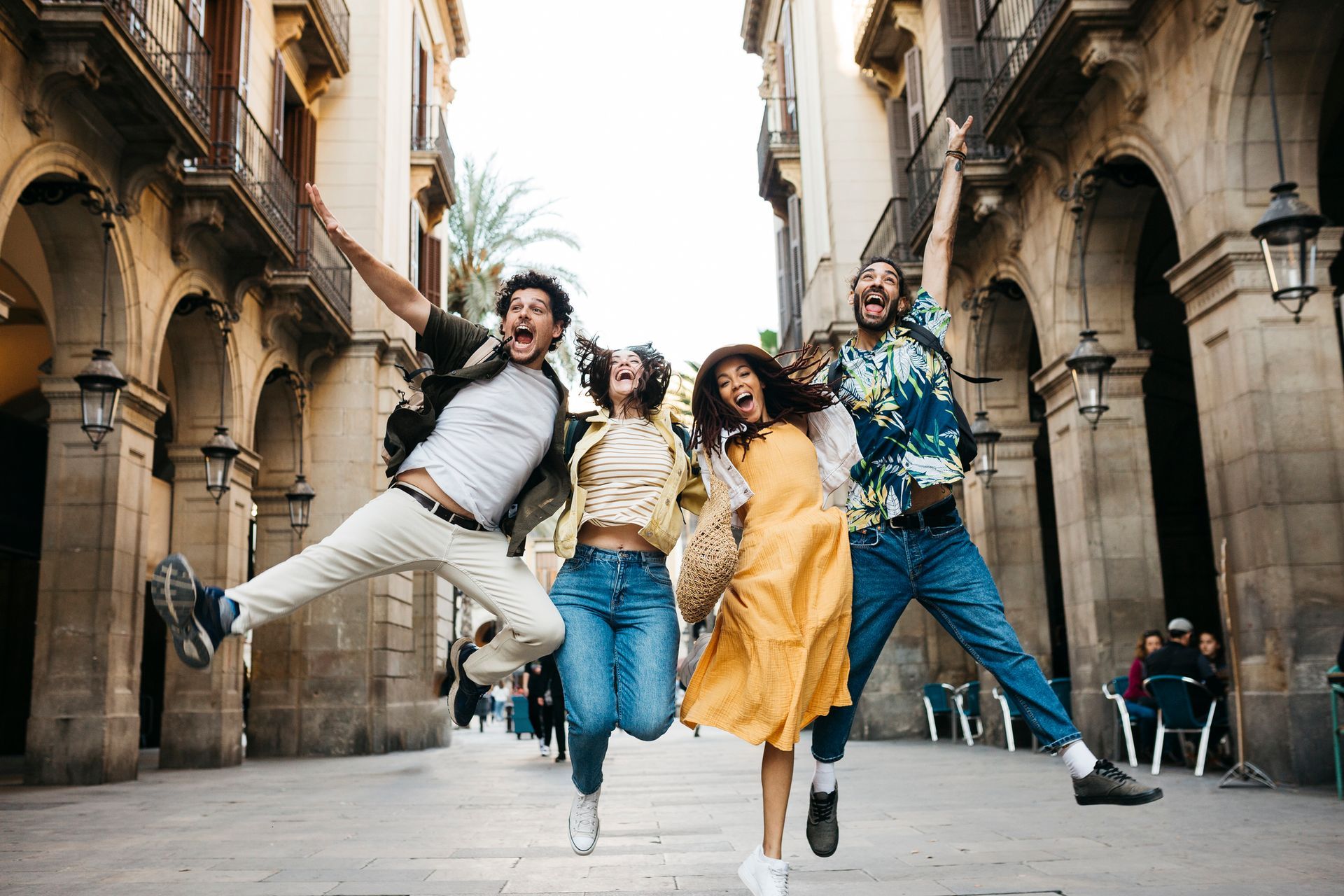 Four people jumping in a city street, arms raised, smiling. Buildings in background.