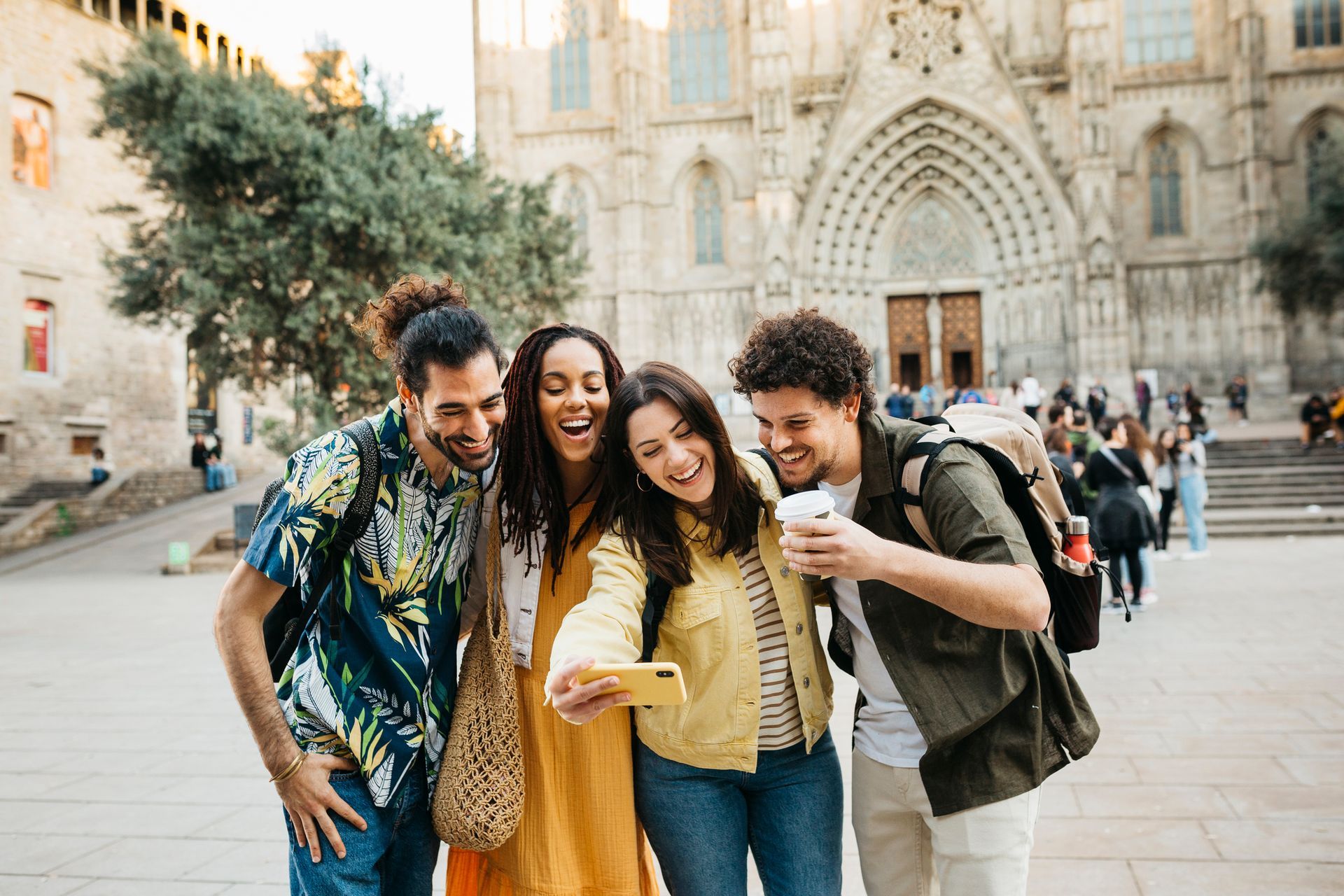 Four friends laughing, taking a selfie in front of a large cathedral.