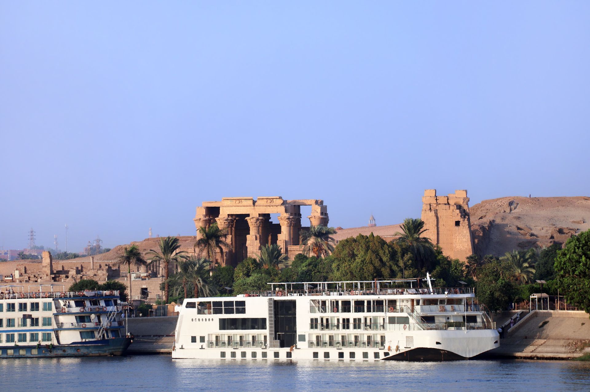 Man in a straw hat taking a photo of a boat and buildings on a river.