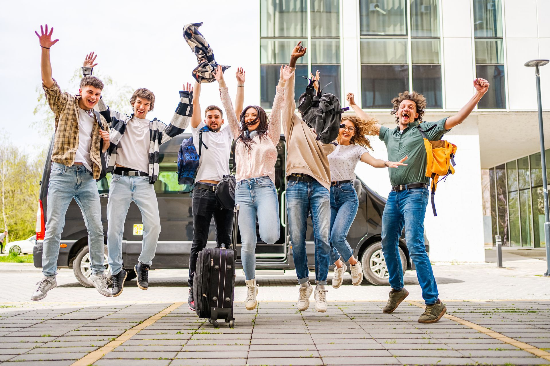 Group of people jumping joyfully in front of a black van, arms raised.