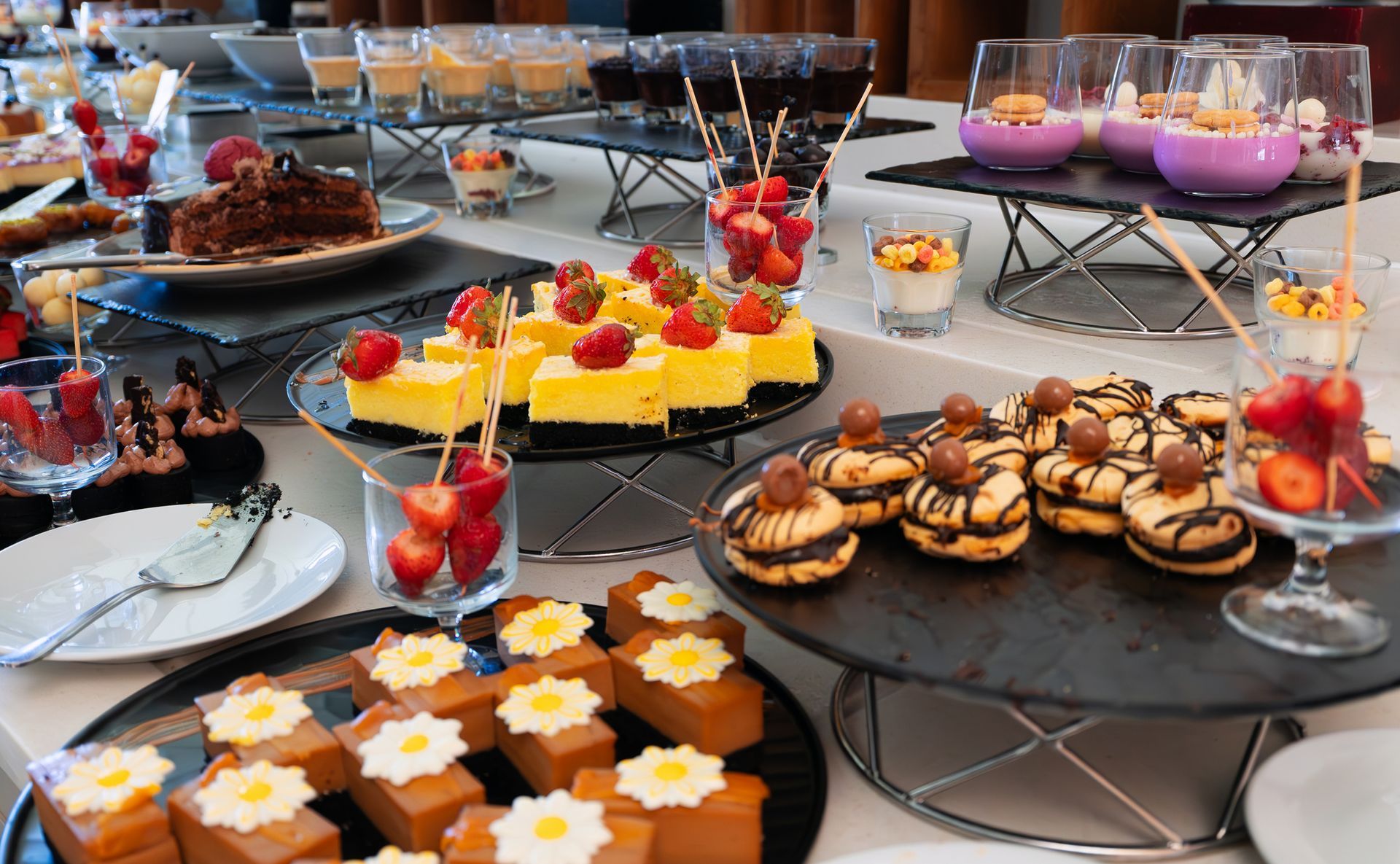 Dessert buffet with various cakes, fruit, and small treats on black serving platters.