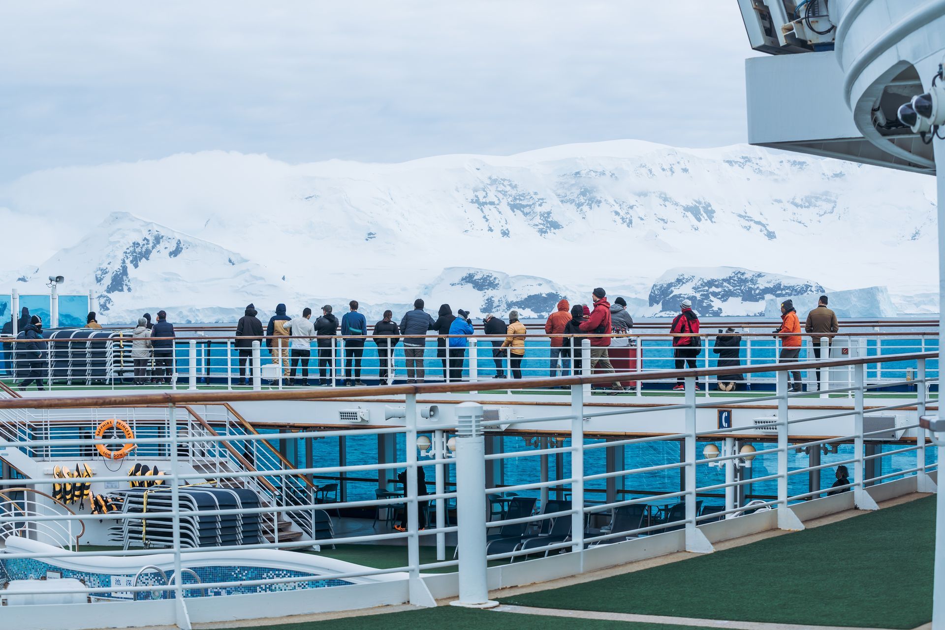 People on cruise ship deck observing snow-covered mountains.