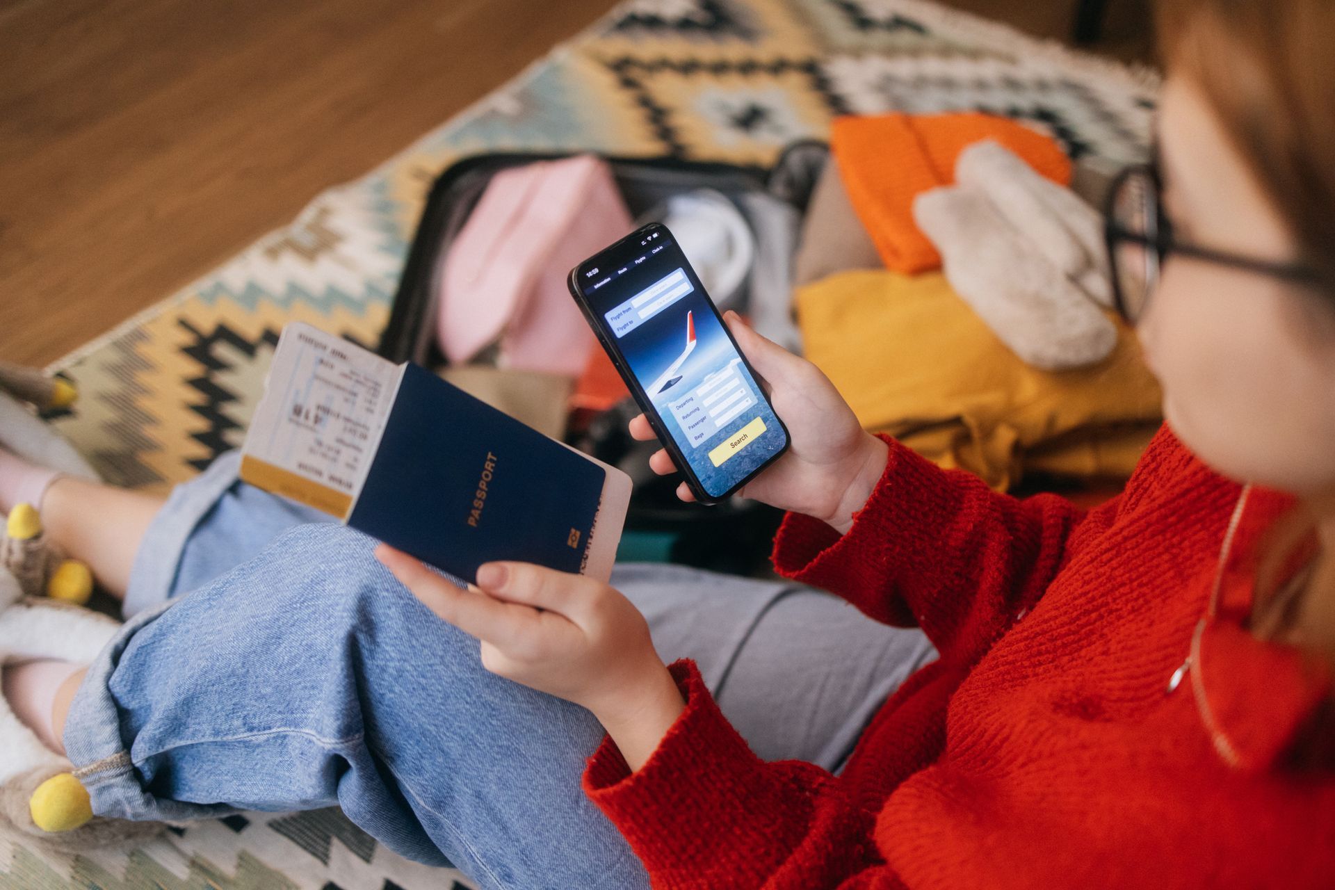 Person holding a phone and passport with a suitcase in the background.