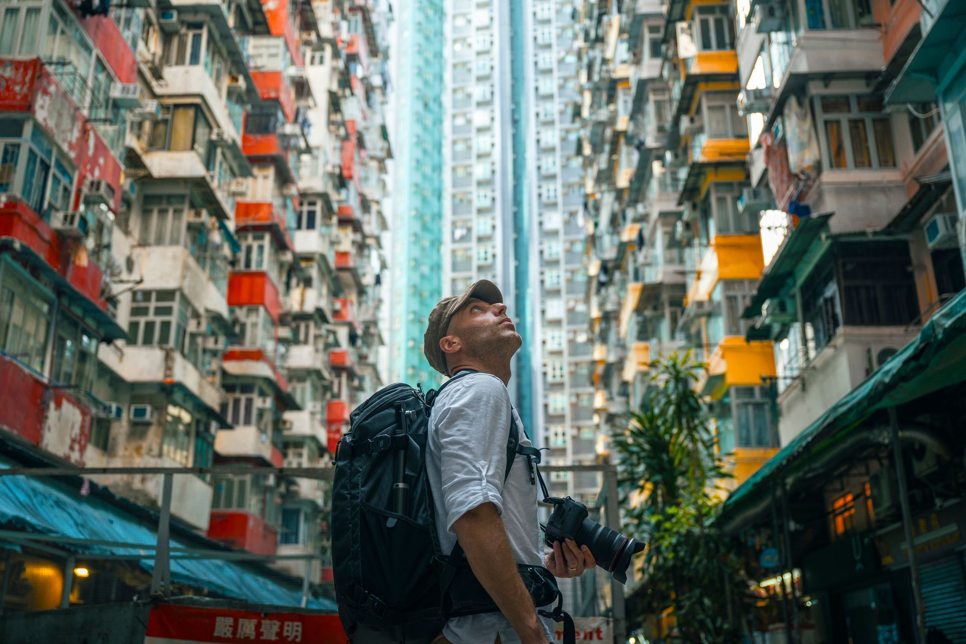 Man with camera looking up at tall buildings. Buildings have many windows, with blue, red, yellow and white colors.