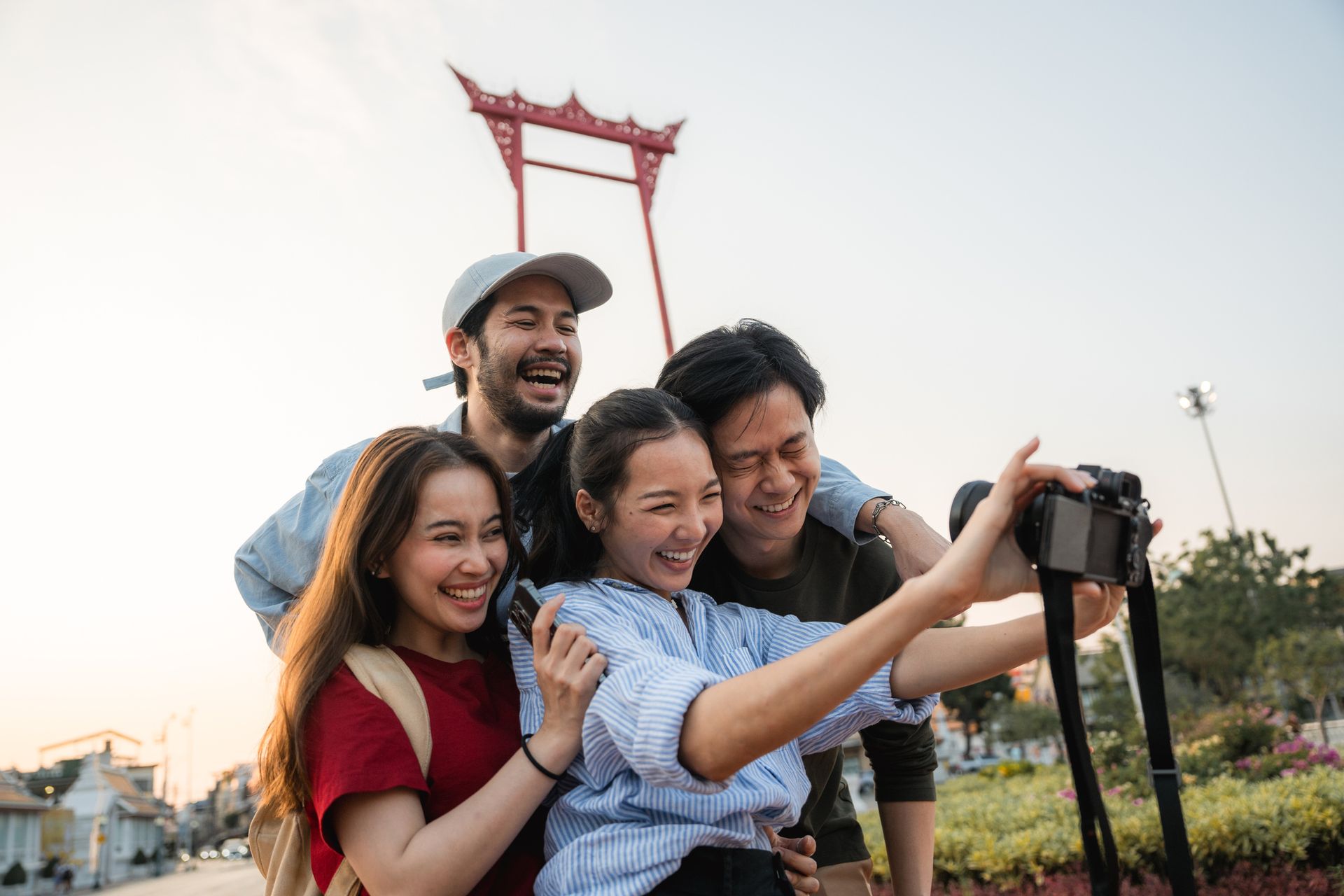 Four people take a selfie in front of a red gate; they smile and laugh, outdoors.
