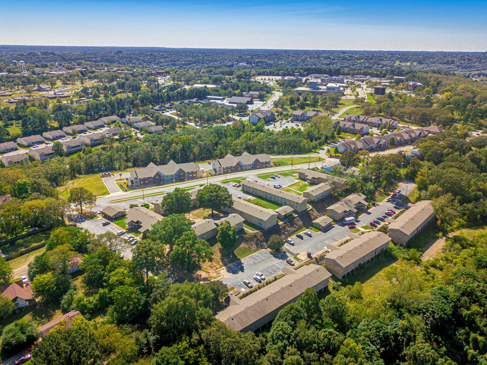 Aerial view of apartment complex surrounded by trees, with a blue sky in the background.