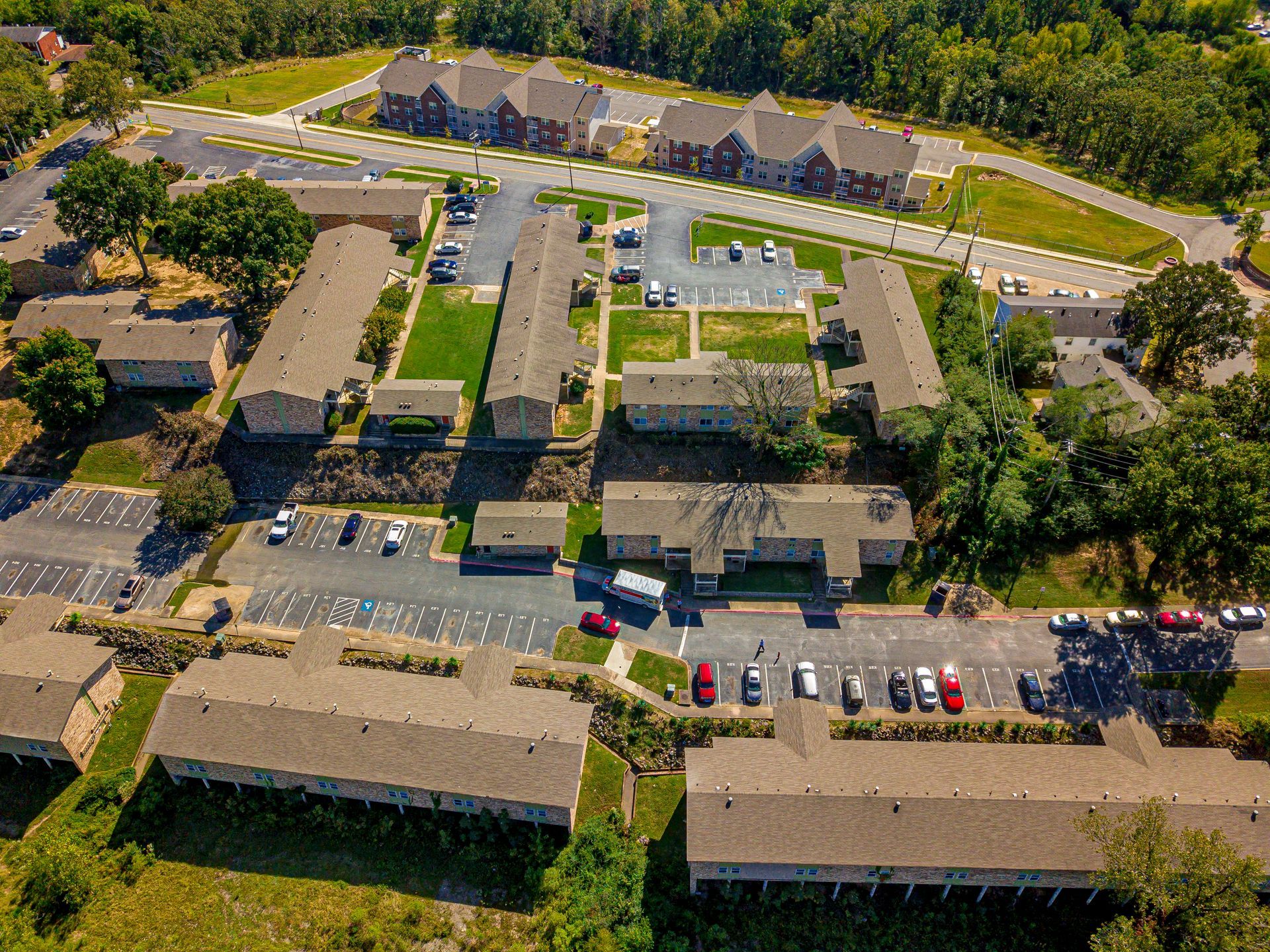Aerial view of an apartment complex with multiple buildings, parking areas, and surrounding green spaces.
