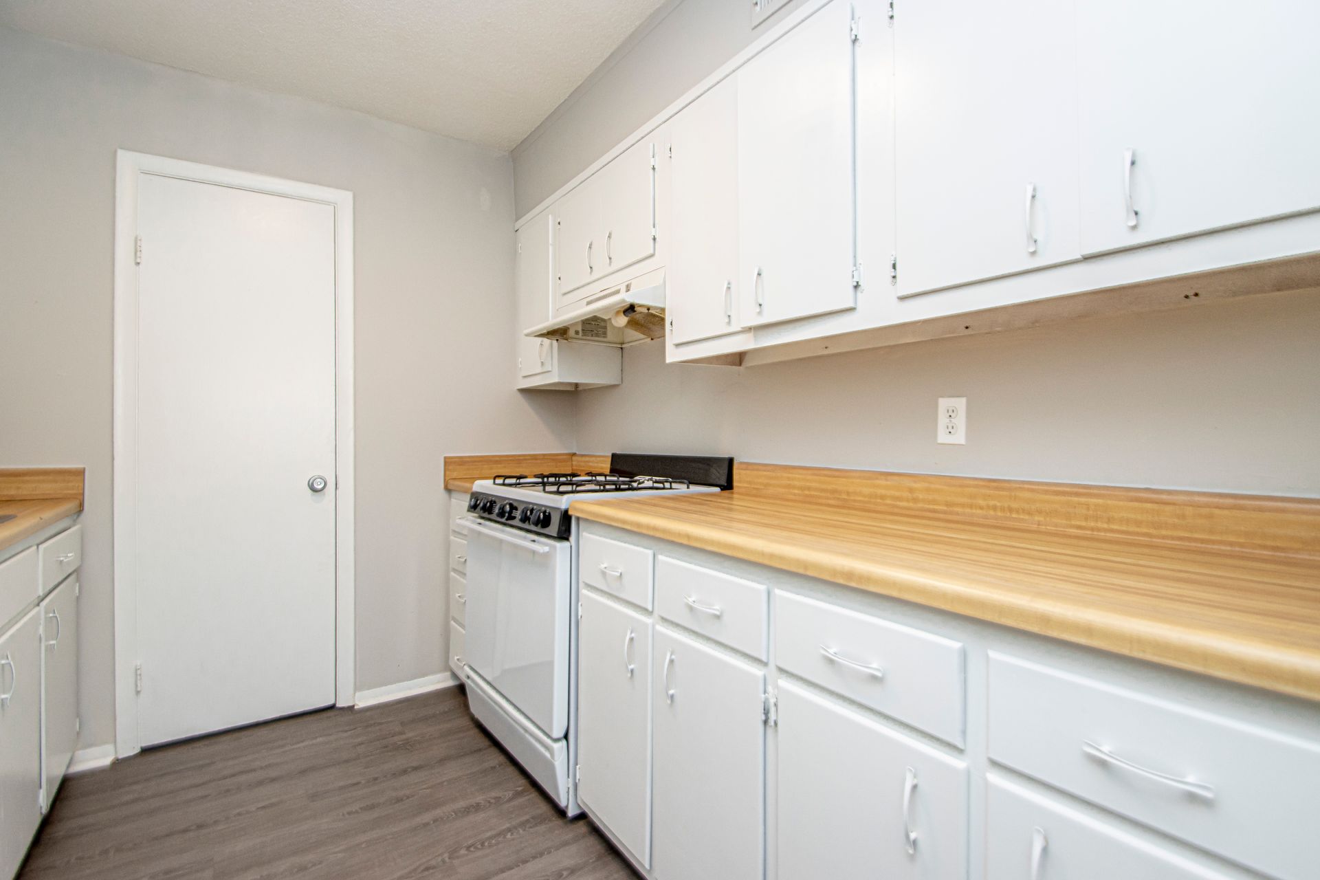 White kitchen with cabinets, stove, and light wood countertops; door on the left.