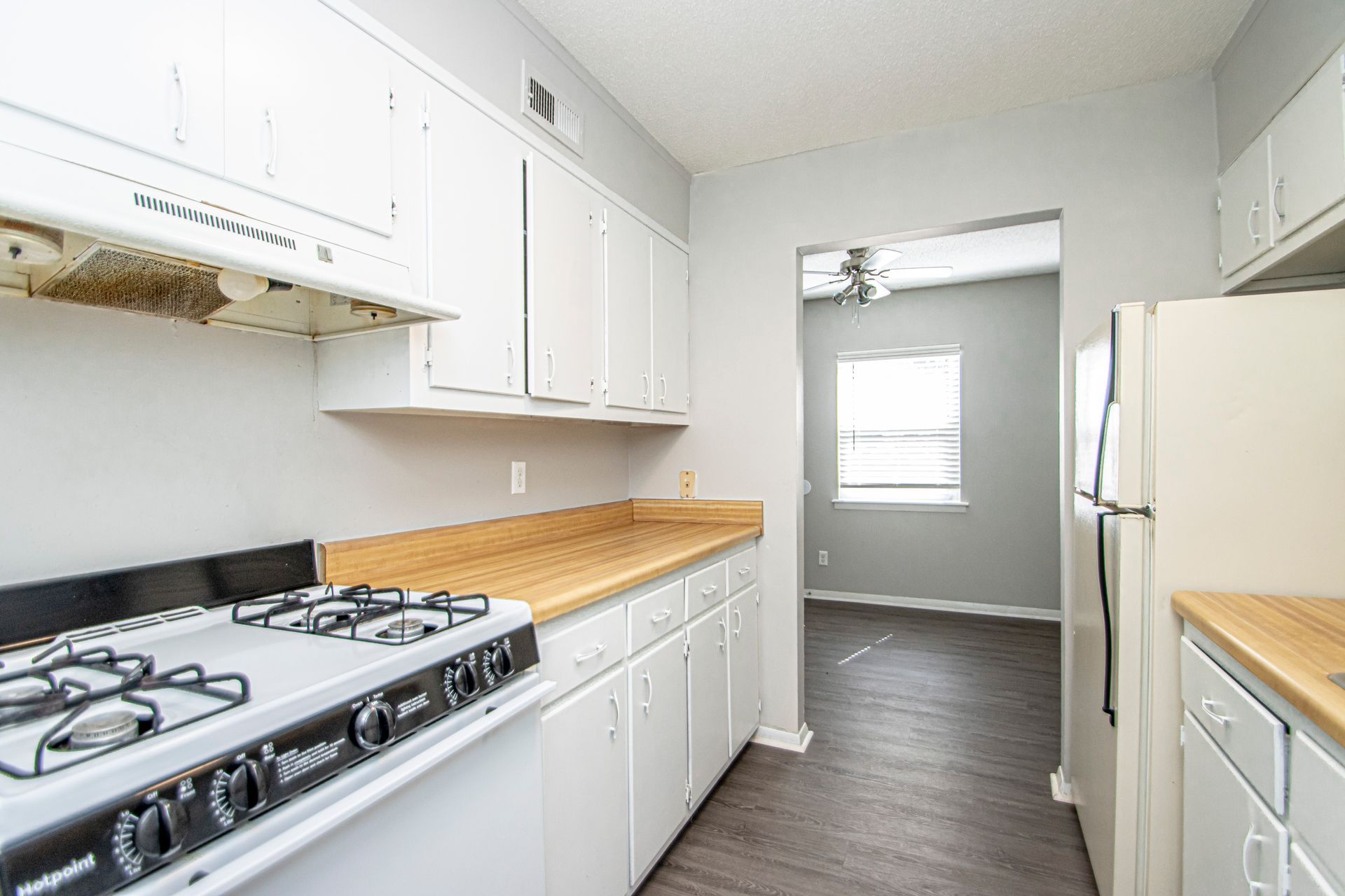 Kitchen with white cabinets, light-colored countertops, and a stove. Open doorway to a living area with a window.