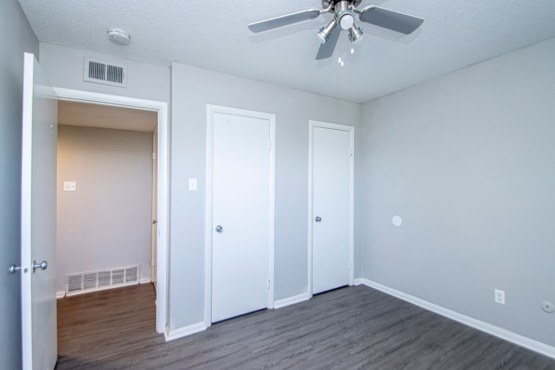 Empty bedroom with grey walls, white doors, a ceiling fan, and a doorway.