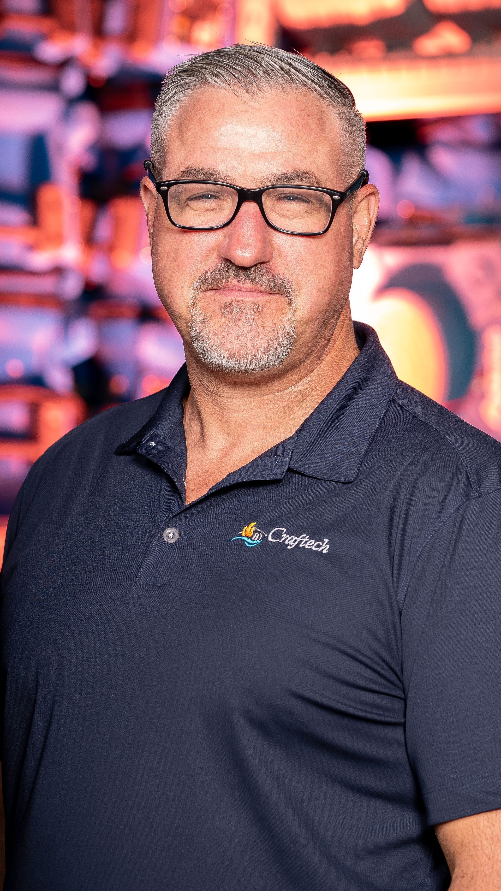 A man with glasses and a beard is wearing a blue polo shirt.