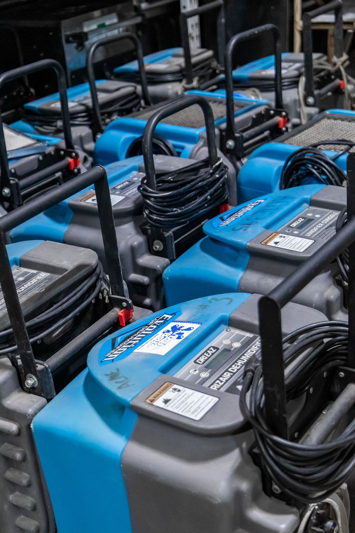 A stack of blue and grey carpet cleaners with black handles and cords.