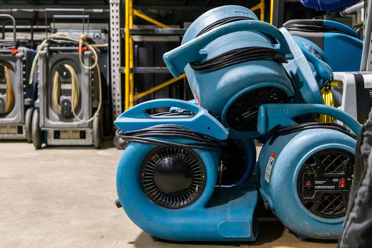 A bunch of blue air conditioners are stacked on top of each other in a warehouse.