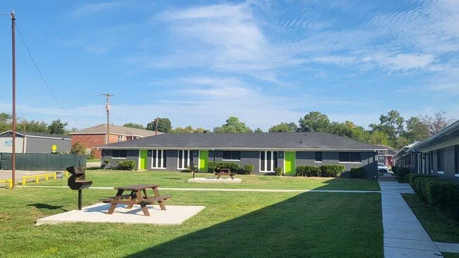 Green and gray apartment buildings with a picnic table on a sunny lawn.