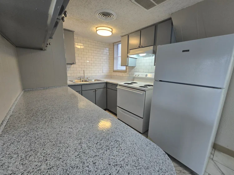 Small kitchen with gray cabinets, white appliances, and a speckled countertop.