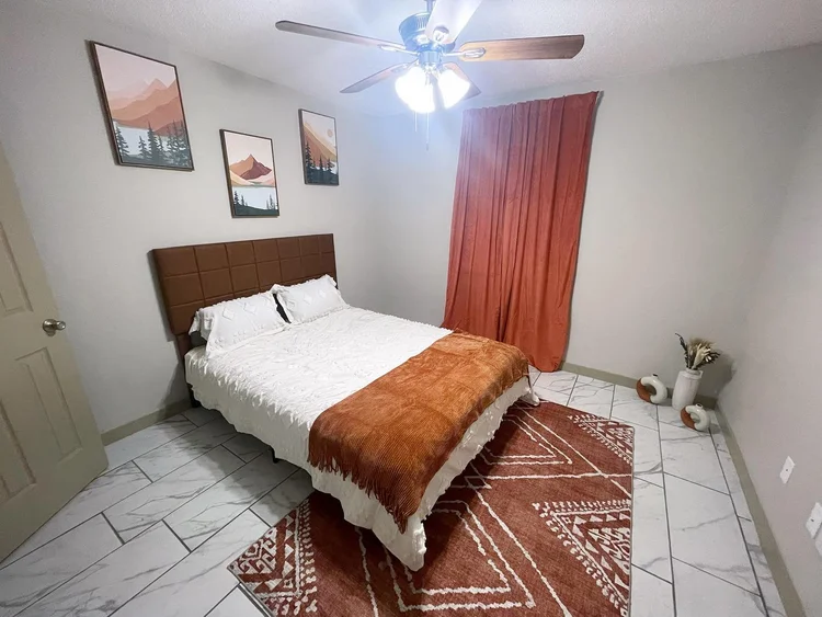 Bedroom with a bed, rug, artwork, and orange curtain.