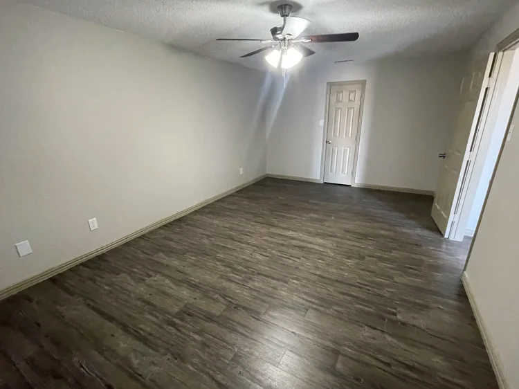 Empty bedroom with dark wood-look flooring, beige walls, and a ceiling fan.