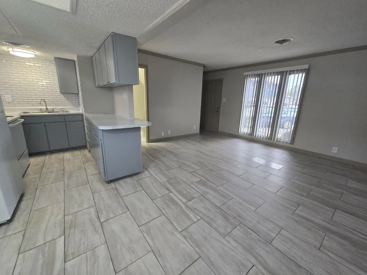 Gray-floored open concept kitchen and living area; light gray cabinets, tiled backsplash, and a sliding glass door.
