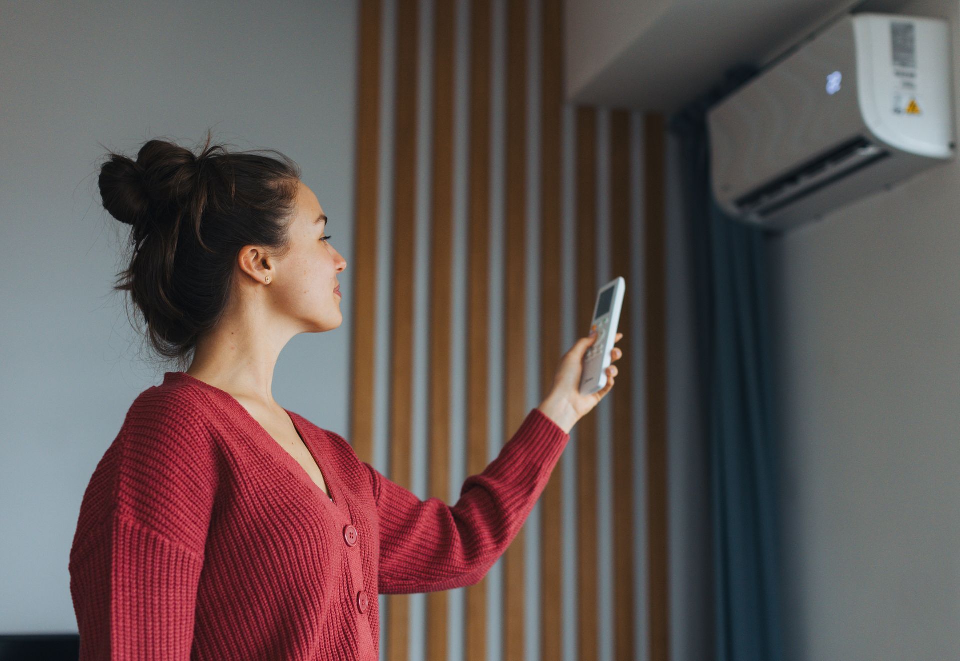 Person in red sweater using remote to control air conditioner on wall.