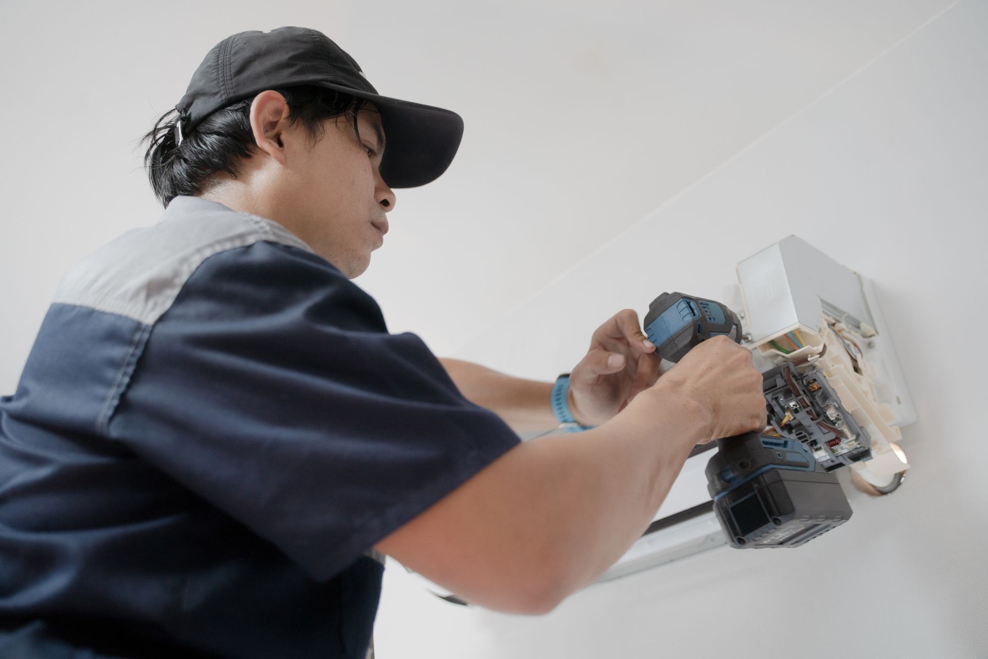 Residential air conditioning contractor fixing a wall mounted air conditioner with a drill. Residential air conditioning contractor fixing a wall mounted air conditioner with a drill.
