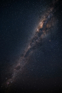 A dense, vertical view of the Milky Way galaxy stretching across a dark, starry night sky with glowing cosmic dust.