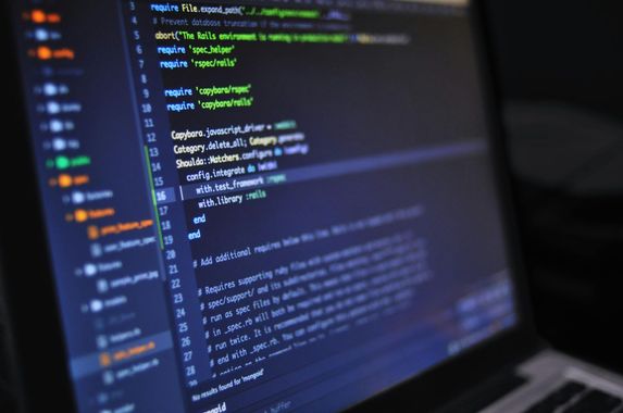 A close-up view of computer code displayed on a laptop screen, showing a dark-themed integrated development environment. AI
