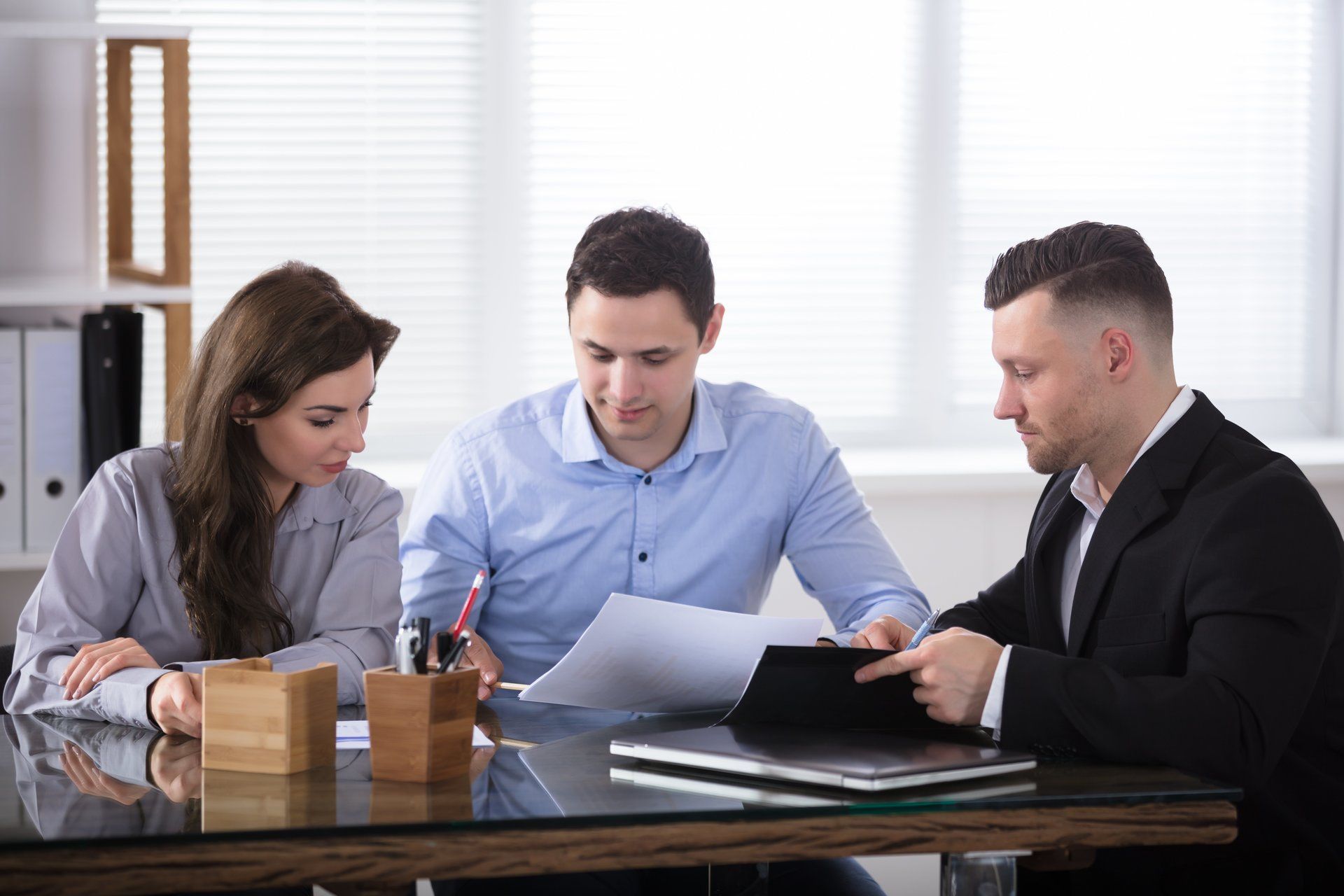A group of people are sitting at a table looking at papers and a tablet.