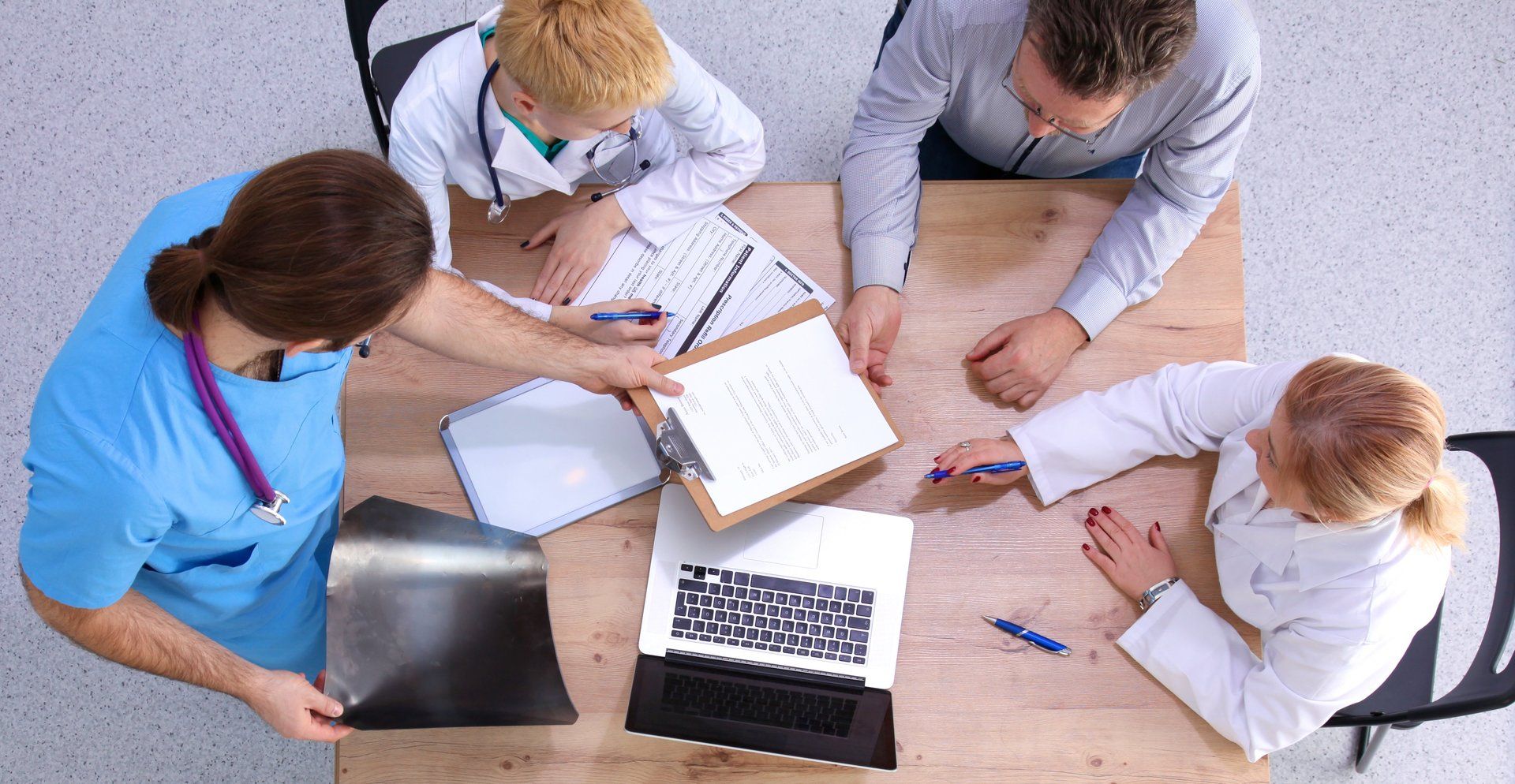 A group of doctors and nurses are sitting around a table with a laptop.