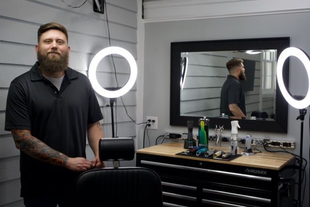 A man with tattoos on his arms is leaning against a wall with his arms crossed.
