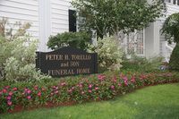 Sign for Peter H. Torello and Son Funeral Home, black with white lettering, in front of a building and landscaping.