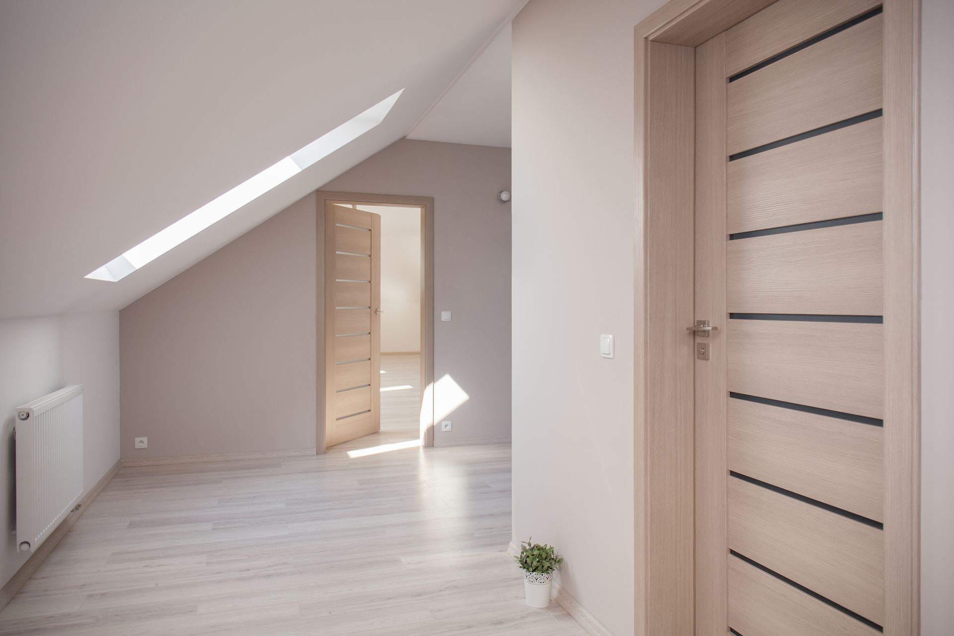 Mansarda vuota con pavimenti in legno chiaro, soffitto spiovente e due porte in legno.