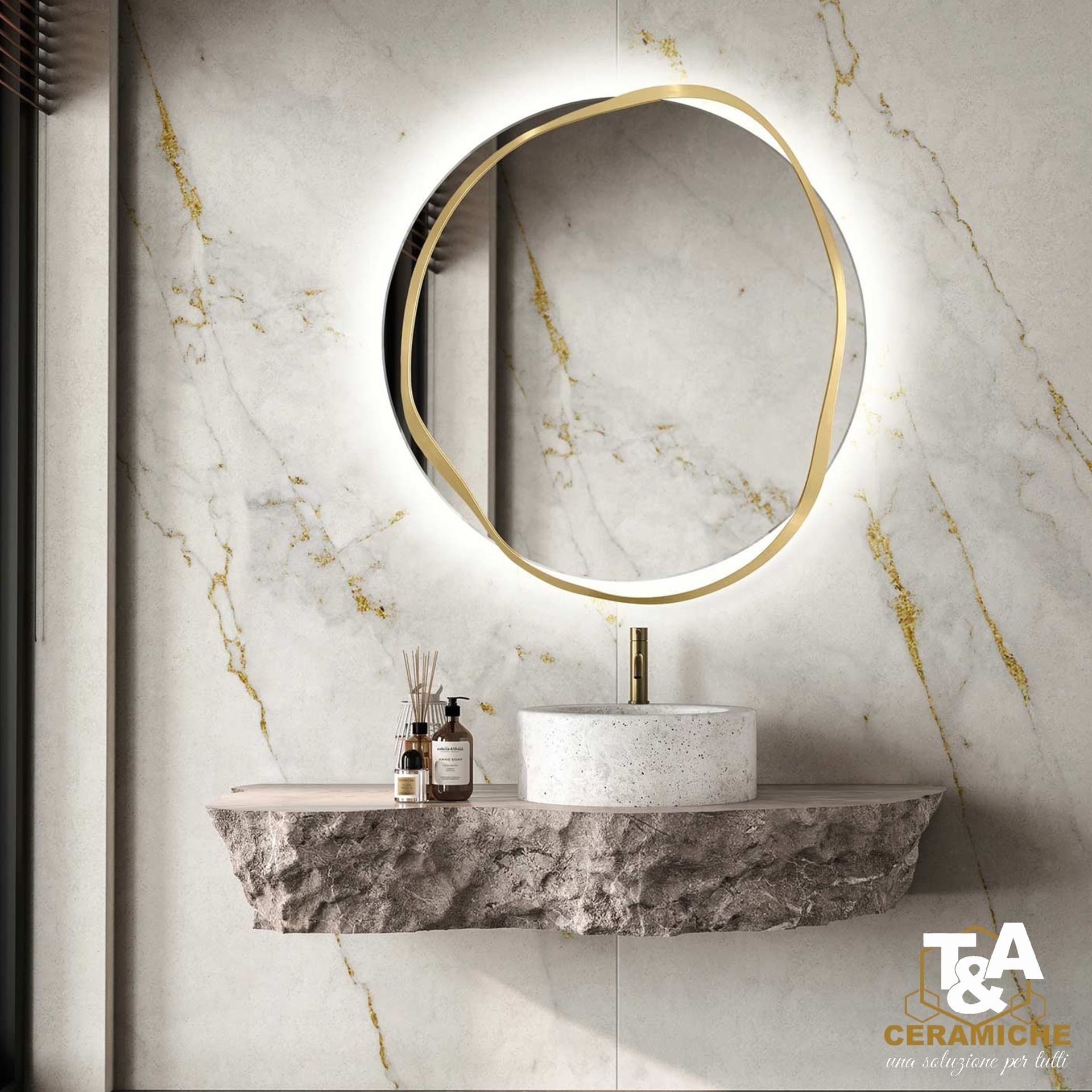 Bagno con specchio con cornice dorata, mensola in pietra sospesa, lavandino in terrazzo e parete effetto marmo.