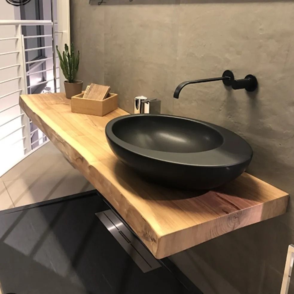 Lavandino del bagno: ciotola ovale nera su lastra di legno, rubinetto nero, parete grigia, cactus, scatola di legno.