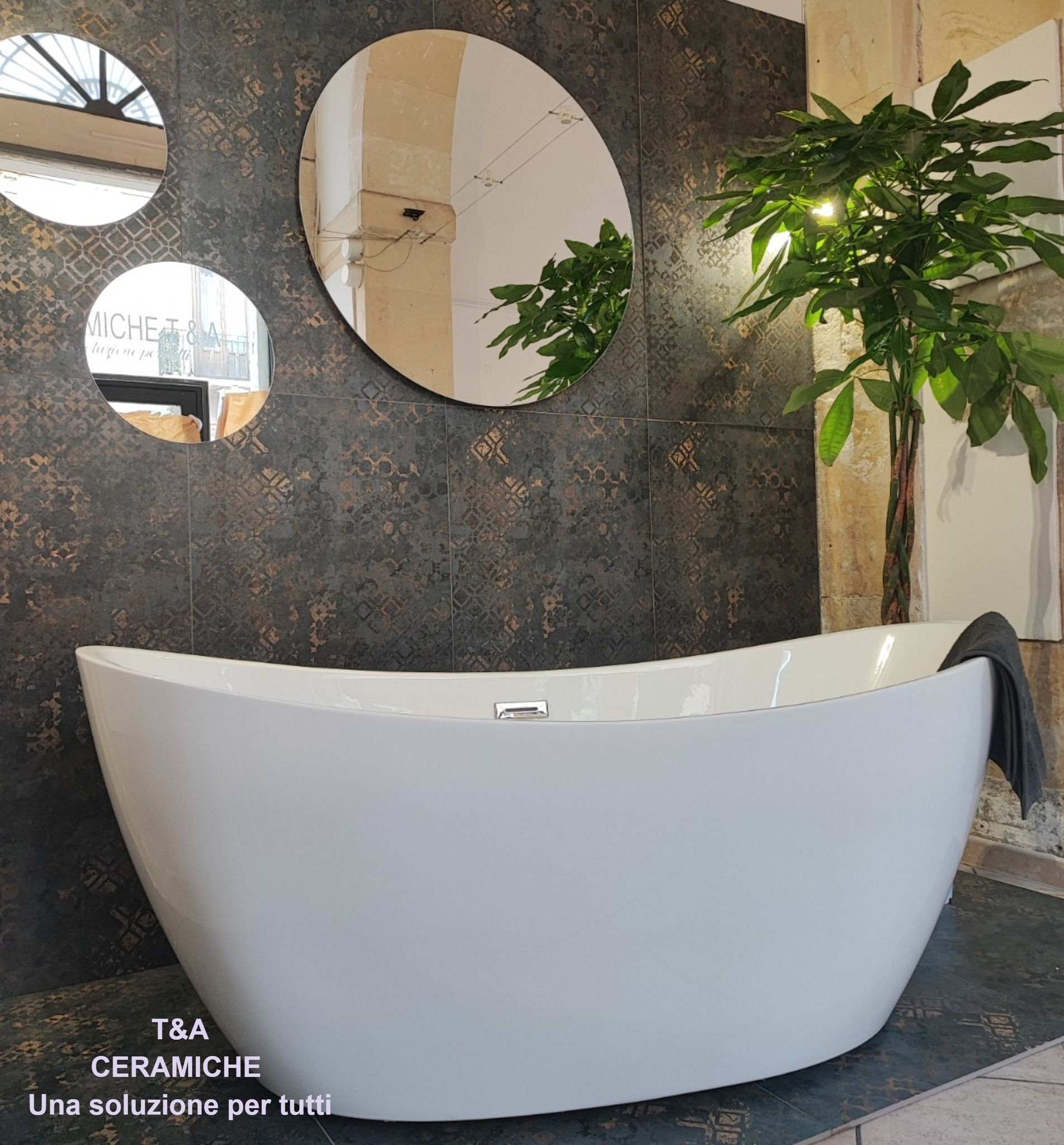 Vasca da bagno bianca in bagno con parete con texture scura, specchi rotondi e pianta.