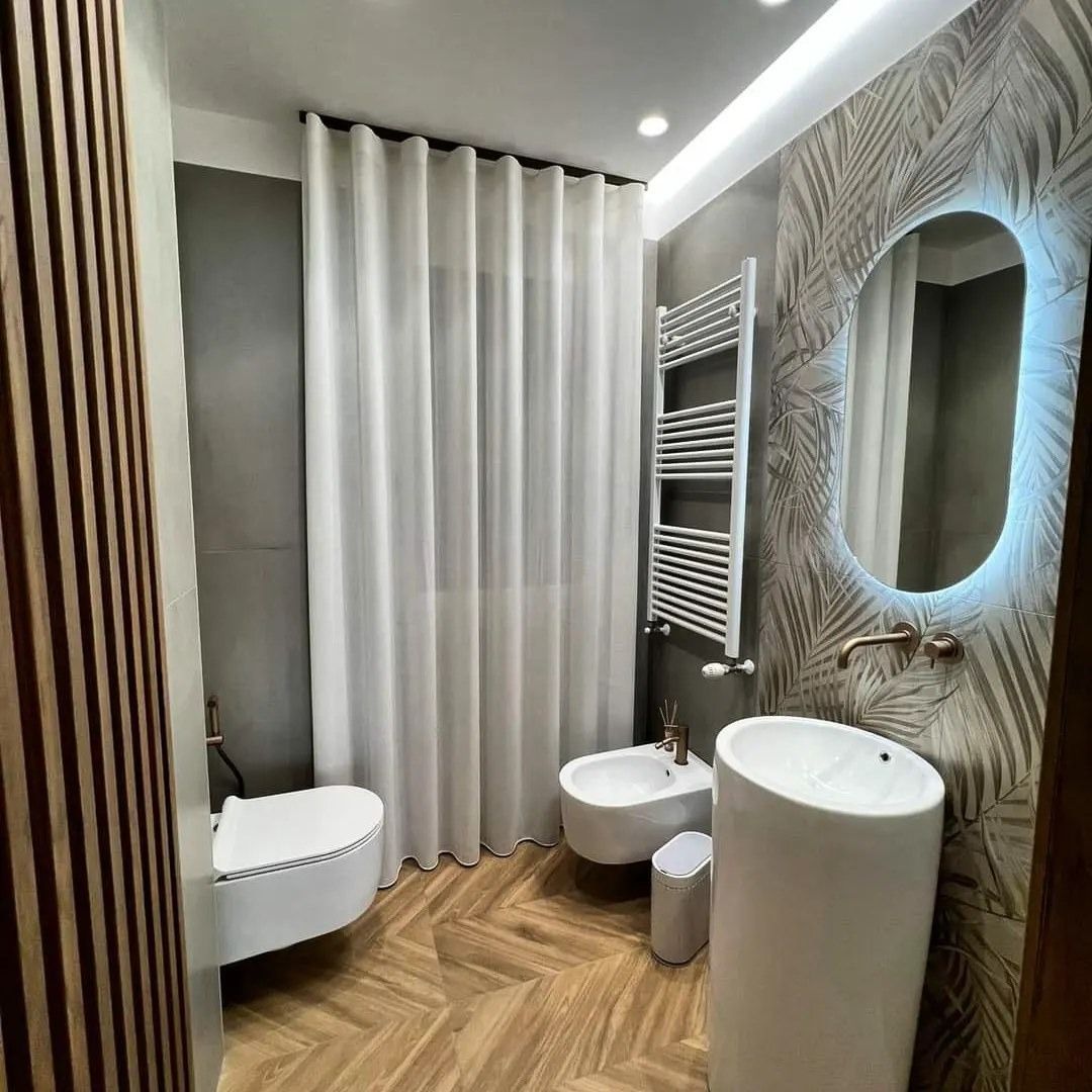 Bagno con tenda bianca, WC, bidet, lavandino e piastrelle decorative alle pareti.