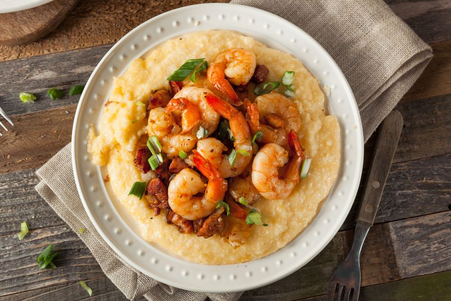 A white plate topped with shrimp and grits on a wooden table.
