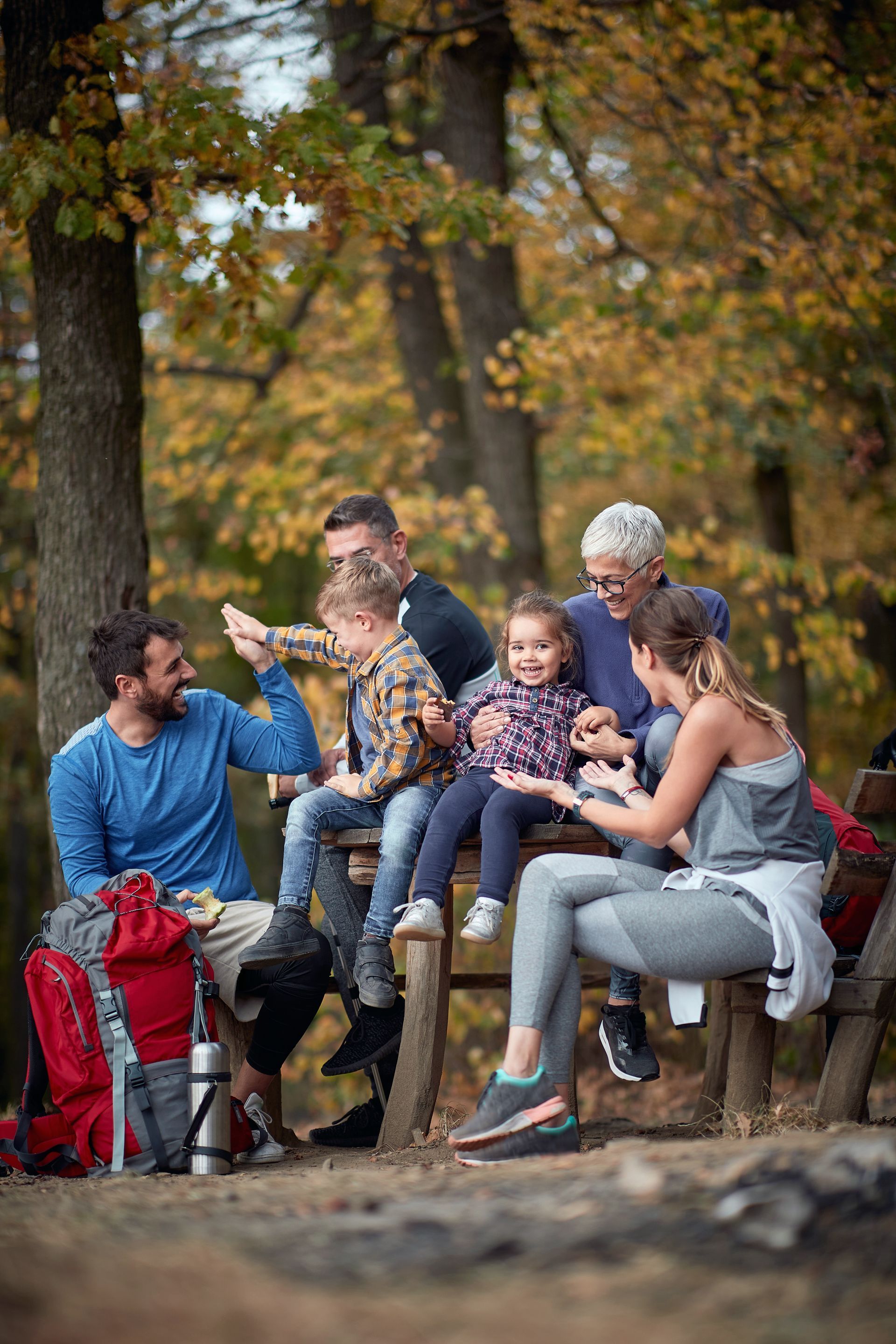A family is sitting on a wooden bench in the woods.