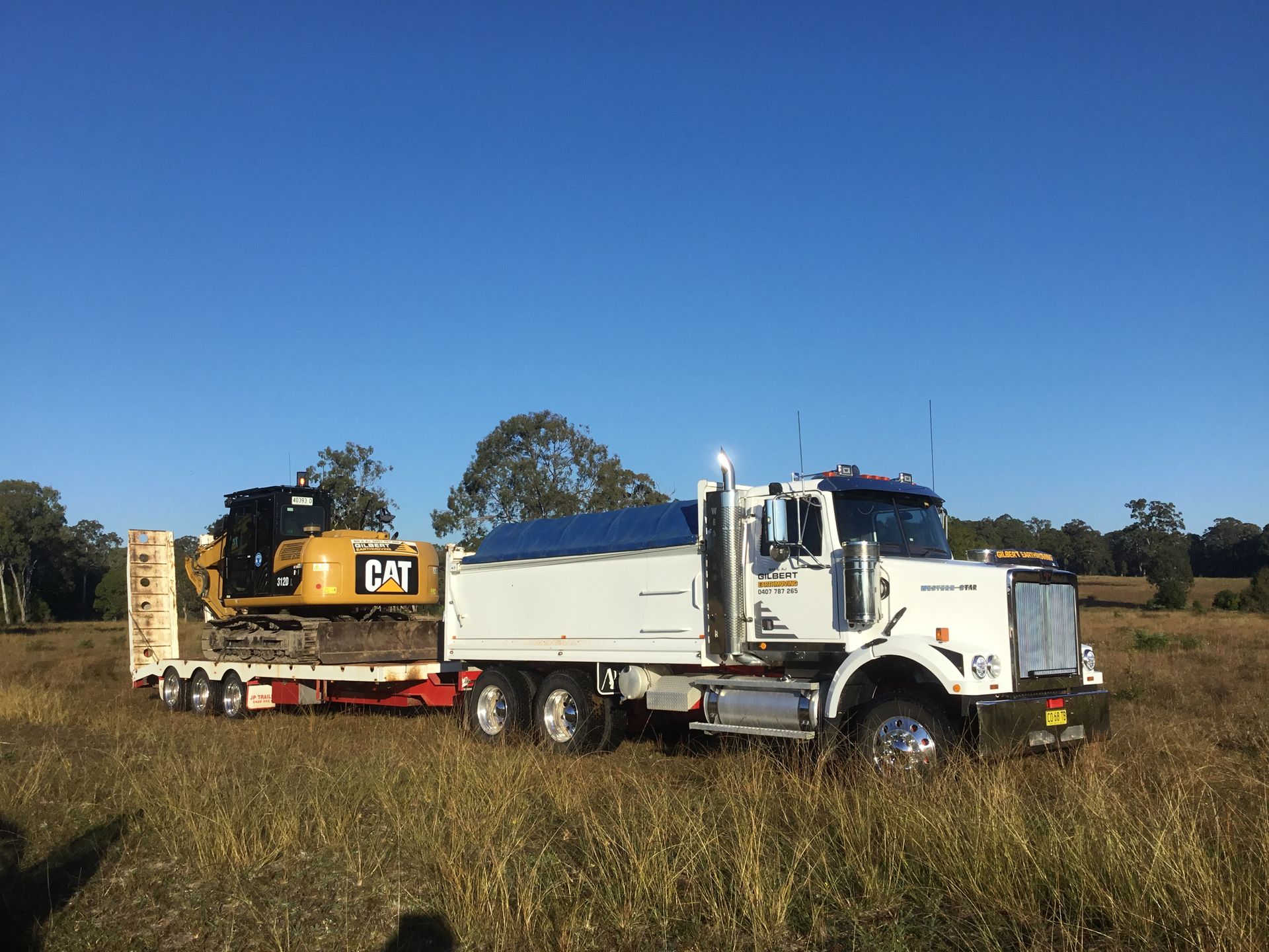 A Yellow Tow Truck is Carrying a Small Excavator — S M & A J Gilbert Earthmoving in Mitchells Island, NSW