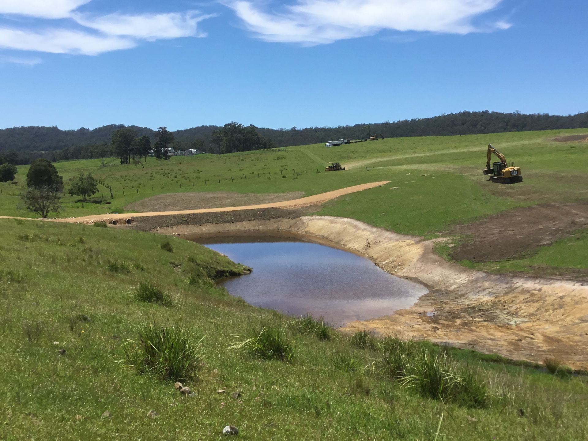 A Small Pond With Earthen Banks Sits in a Grassy Field Under a Blue Sky — S M & A J Gilbert Earthmoving in Mitchells Island, NSW