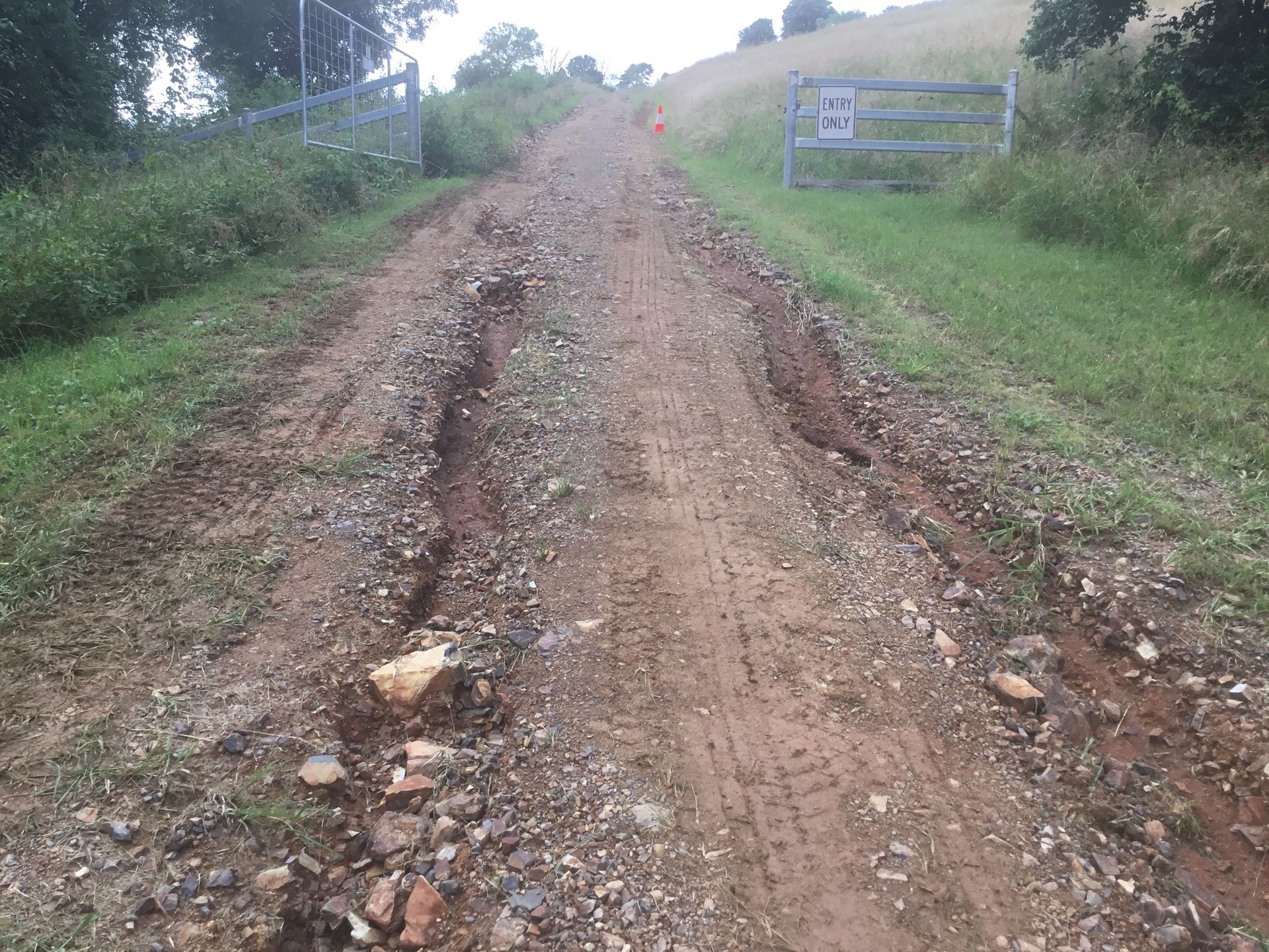 Long Gravel Road With Tire Tracks Leading Uphill, Flanked by Grass — S M & A J Gilbert Earthmoving in Mitchells Island, NSW