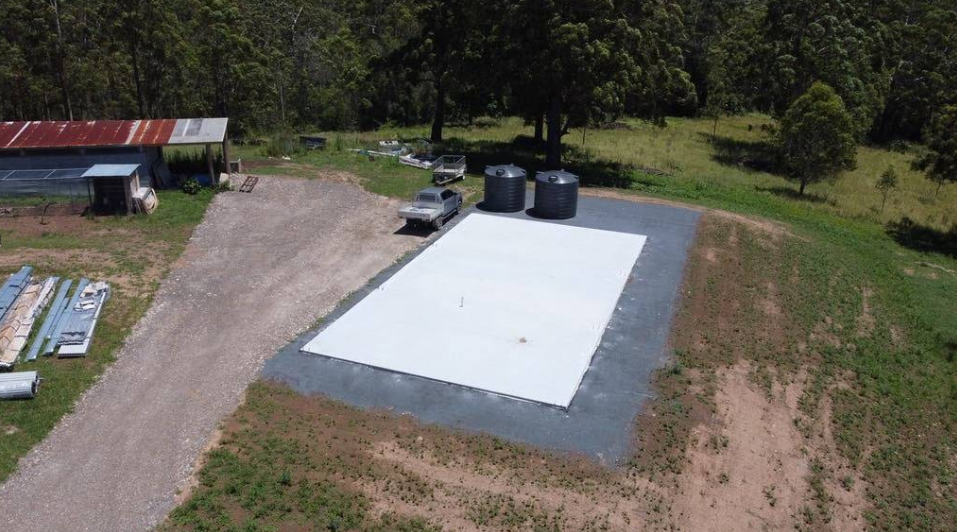 An Aerial View of a Rural Property With a Large White Roof, Two Water Tanks — S M & A J Gilbert Earthmoving in Mitchells Island, NSW