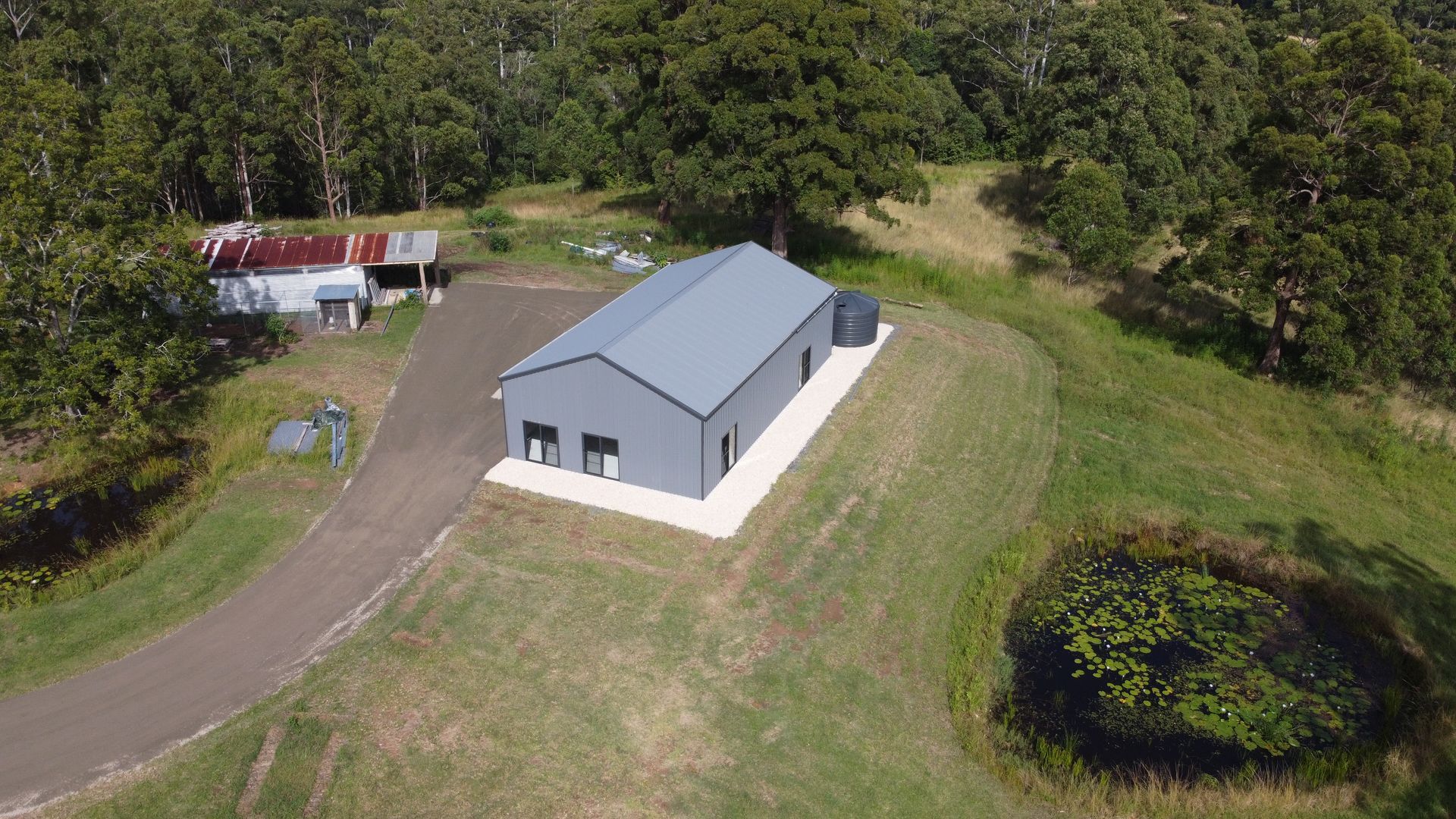 Aerial View of a Gray Hard Metal Building With a Gravel Base, Situated Near a Pond and a Wooded Area — S M & A J Gilbert Earthmoving in Mitchells Island, NSW